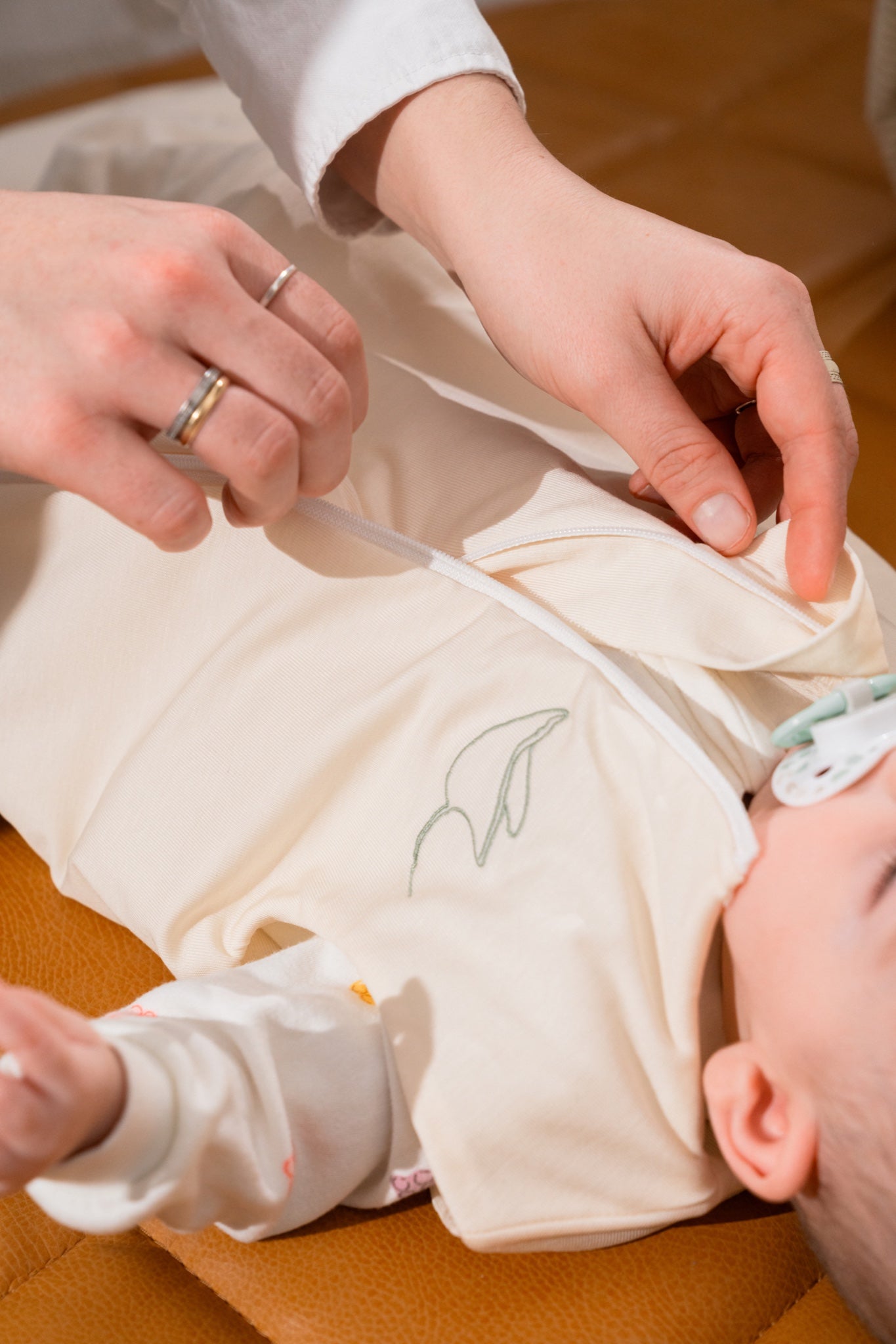 Parent's hands closing the central zip of the Nömad sleep sack on baby
