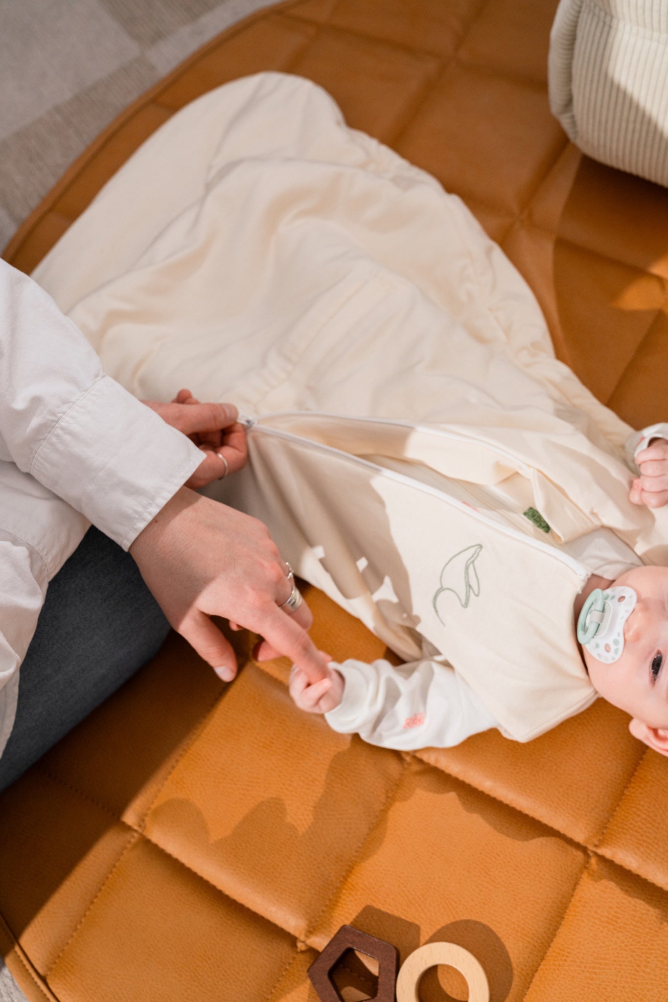 Parent opening the central zip of the Nömad sleep sack, baby lying on a play mat